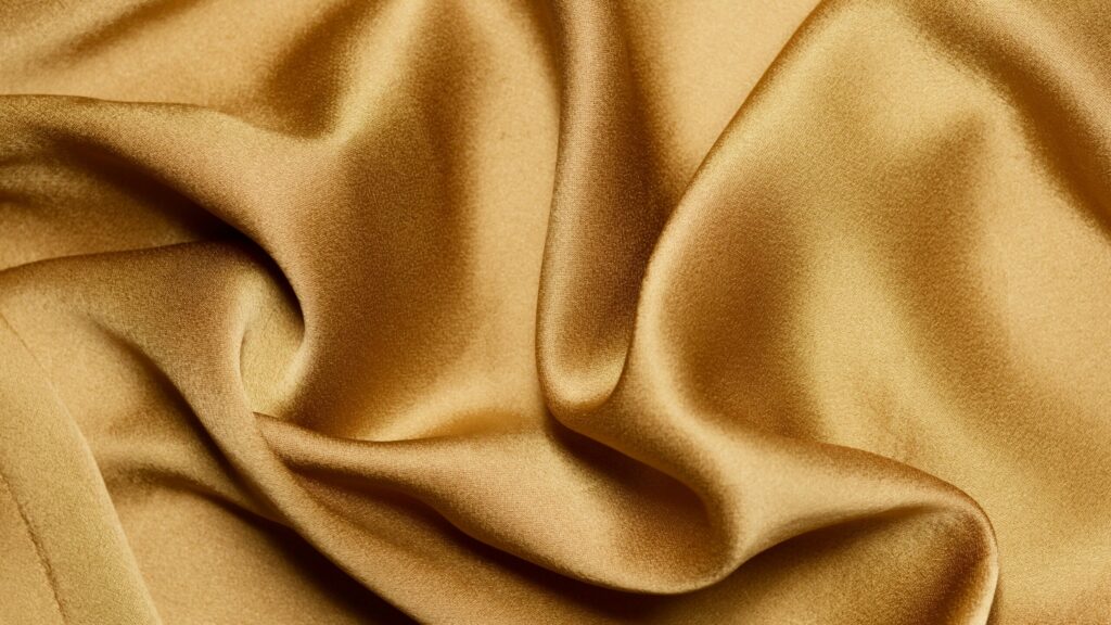 Luxurious close-up of gold silk fabric with elegant folds and texture.